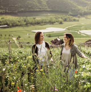 Fifth-generation sisters Karoline and Julia Walch of Alto Adige’s Elena Walch smile at each other while standing casually among their high-elevation vineyards.