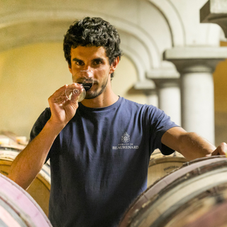Victor Coulon with one hand resting on a wine barrel and his nose in a wine glass.
