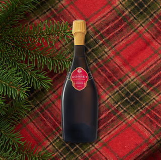 Bottle of Gosset Grande Réserve Brut Champagne placed on a red-and-green plaid fabric with evergreen branches along the left side.