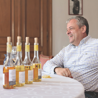 Winery Director Zoltán Kovács of Royal Tokaji smiling while looking into the distance, with a row of Royal Tokaji bottles arranged on the table in front of him.