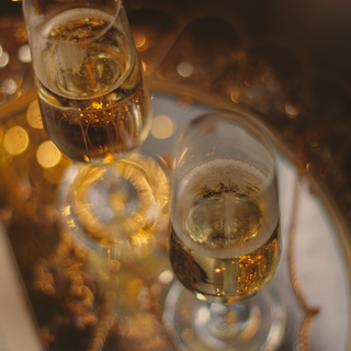 Overhead view of two champagne flutes on a mirrored tray, softly out of focus.