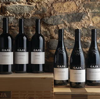 A lineup of GAJA wine bottles displayed against a faded brick wall.