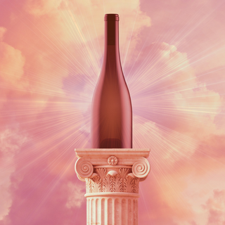Unlabeled wine bottle displayed atop a classical stone column, with radiant light beams and pink clouds in the background.