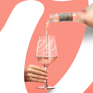 Rosé Prosecco being poured from a chilled bottle into a sparkling wine glass held by a hand, set against a soft pink graphic background.