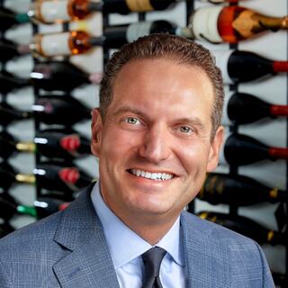 Vice President Business Development Michael Traverso poses for his headshot in the Wilson Daniels wine cellar. He is smiling and wearing a blue-colored suit.