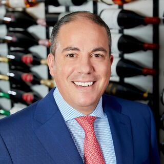 Wilson Daniels President Rocco Lombardo headshot. He is wearing a blue blazer and red tie and smiling in the Wilson Daniels wine cellar.
