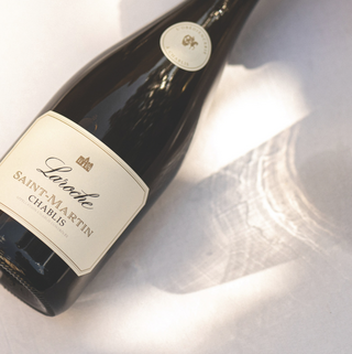 Bottle of Domaine Laroche's Saint-Martin Chablis wine photographed diagonally on a white surface, with sunlight casting a rippling reflection beside the bottle.