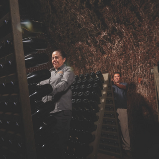Two winery workers stand among wooden riddling racks filled with sparkling wine bottles inside the rock-lined Schramsberg caves.