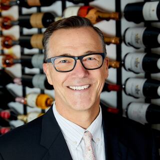 Vice President of Marketing Scott Ehrlich poses for his headshot in the Wilson Daniels wine cellar. He is smiling and wearing a dark-colored blazer.