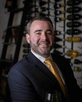 A headshot of Michael Tobin in the Wilson Daniels wine cellar. He is smiling and wearing a yellow tie and a blue blazer.