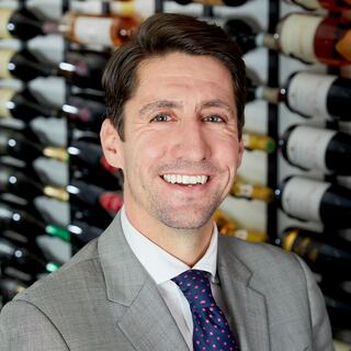 Wilson Daniels Executive Vice President of Wholesale and Operations Kevin Murphy headshot. He is wearing a light-colored blazer and blue tie and smiling in the Wilson Daniels wine cellar.