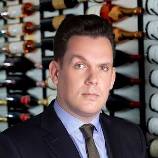 Vice President of the Private Client Group Services Adam Schneider poses in the Wilson Daniels wine cellar in a dark suit.