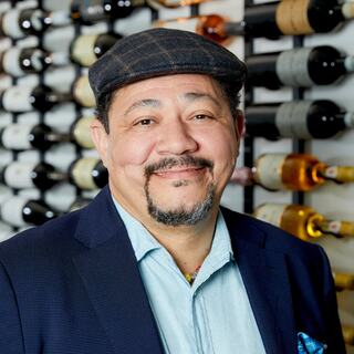 Director of Education William Davis poses for his headshot in the Wilson Daniels wine cellar. He is smiling and wearing a cap and a blue blazer.