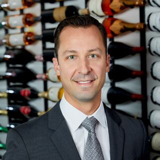 Midwest Division Vice President Marc Nuara poses for his headshot in the Wilson Daniels wine cellar. He is smiling and wearing a dark-colored suit.