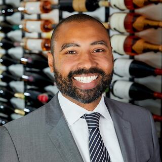 Southern Division Vice President Kim Wood is posing for his headshot in the Wilson Daniels wine cellar. He is smiling and wearing a gray suit and a striped blue tie.