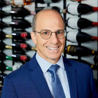Finance Vice President James DiCicco poses for his headshot in the Wilson Daniels cellar. He is smiling and wearing a blue suit and glasses.