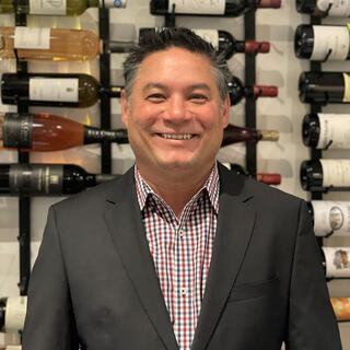 Vice President of Western Division Andy Lum poses for a headshot in the Wilson Daniels wine cellar. He is wearing a checkered button down and a dark gray blazer.