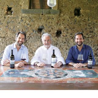 The Benanti family sit at a table, holding wine glasses and wine bottles.