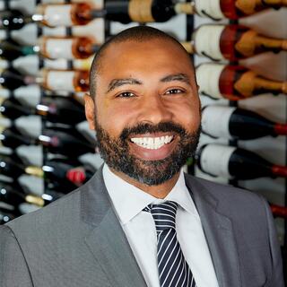 Kim Wood poses for his headshot in the Wilson Daniels wine cellar. He is smiling and wearing a gray suit.