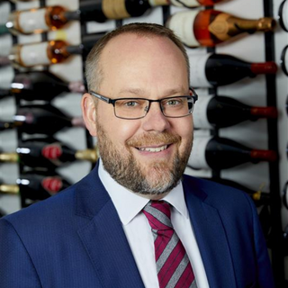 A headshot of Jerred Wolff in the Wilson Daniels wine cellar. He is smiling and has glasses.