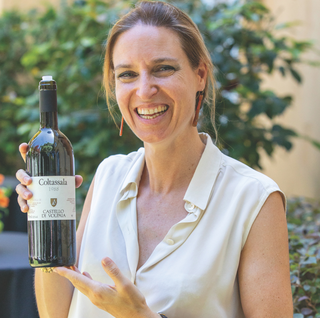 Federica Mascheroni Stianti of Castello di Volpaia smiling while holding an older vintage of Coltassala; her hair is tied back.