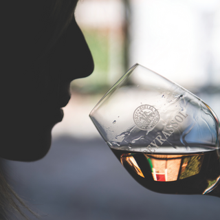 Silhouette of a woman in profile sipping from a Peyrassol-branded wine glass.